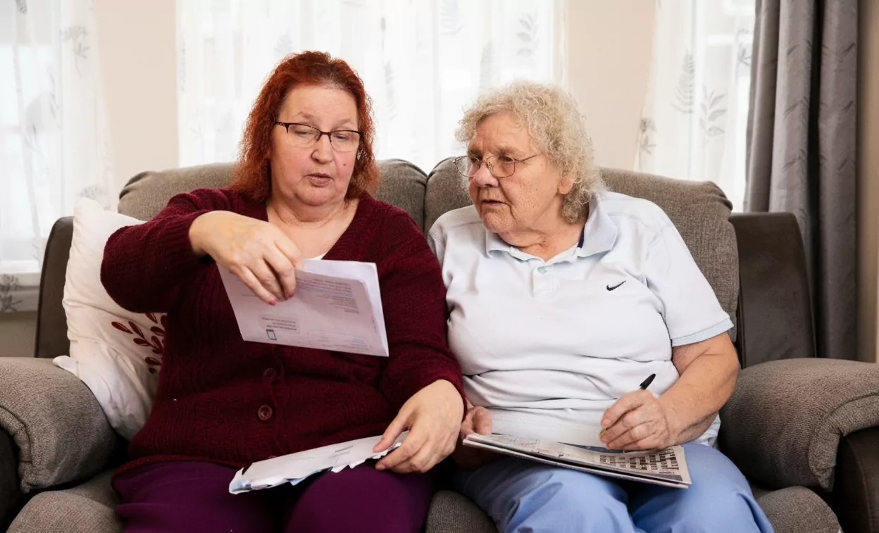 Two older women sitting together on a couch looking at a piece of paper