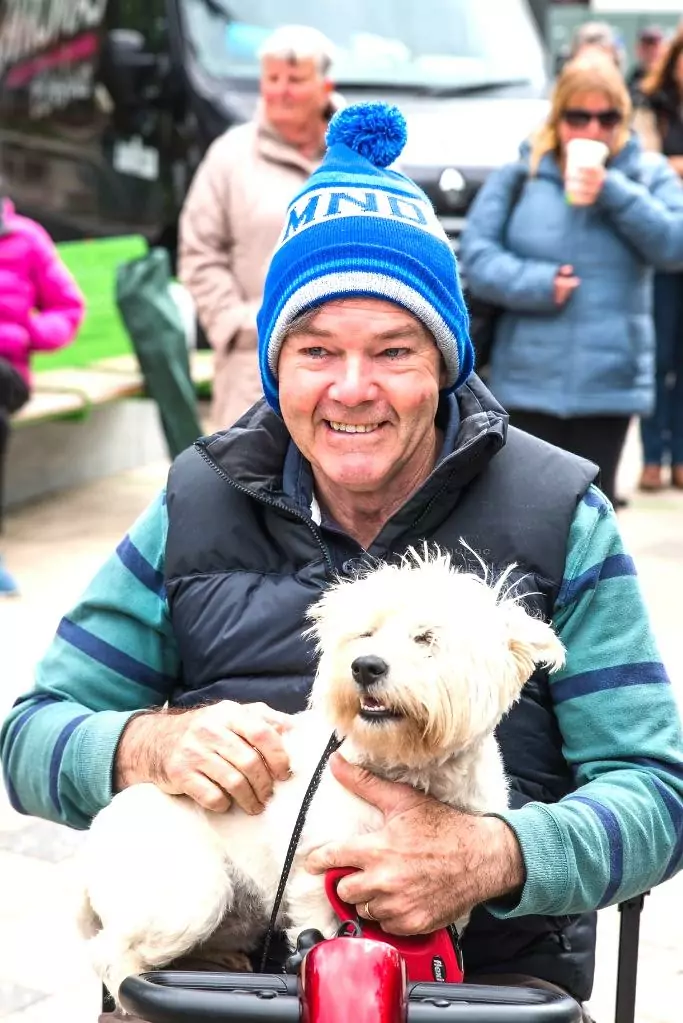 An older man smiling in a wheelchair with a white dog on his lap