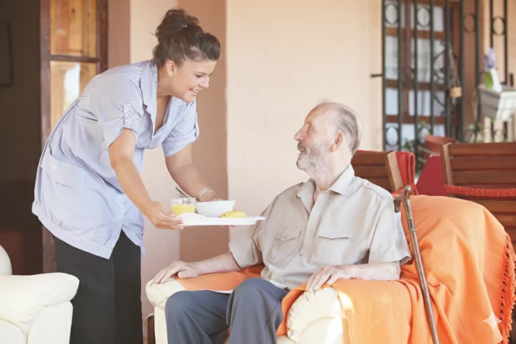 A female carer from Community Care TASMANIA serving an older man his dinner on a tray