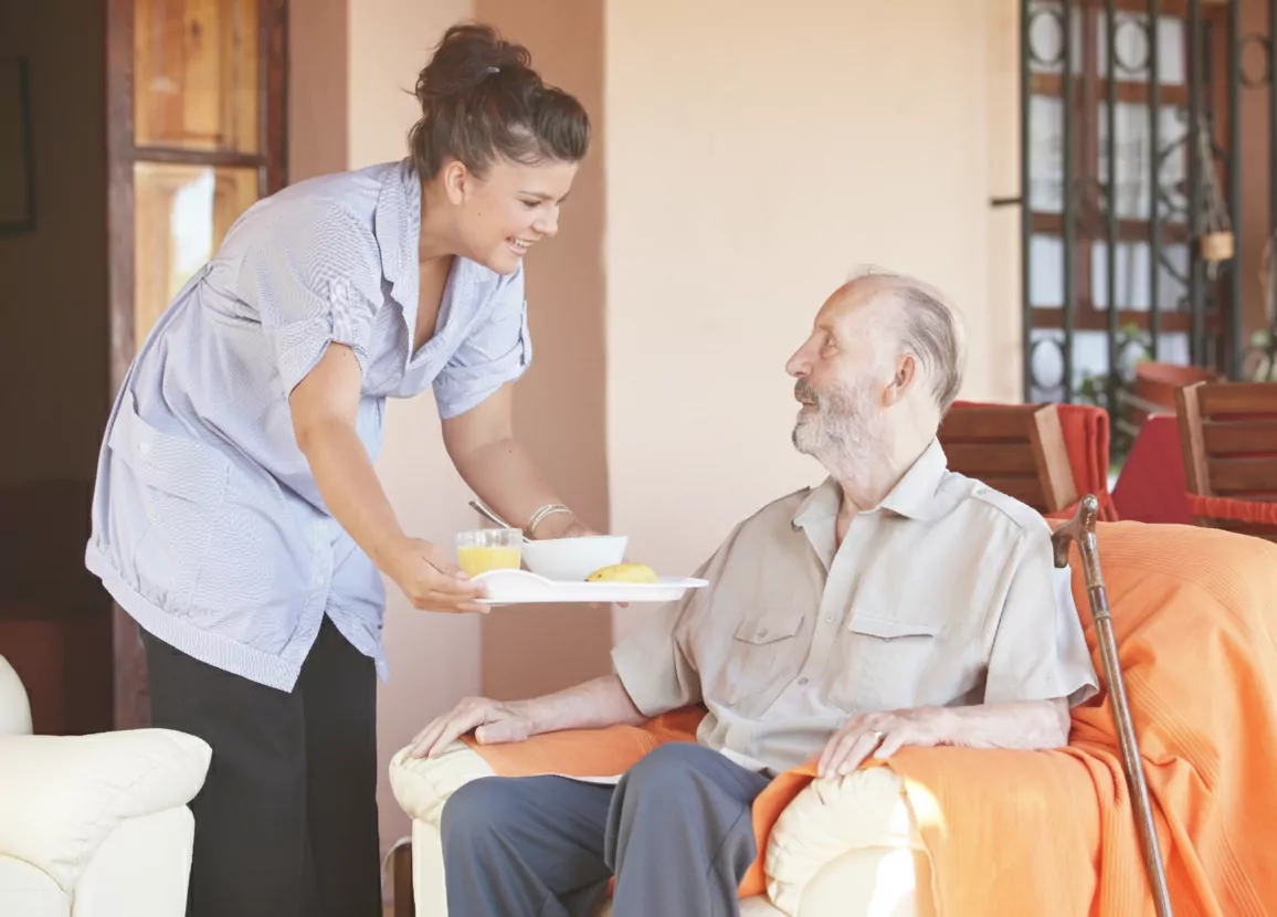 A female carer from Community Care TASMANIA serving an older man his dinner on a tray