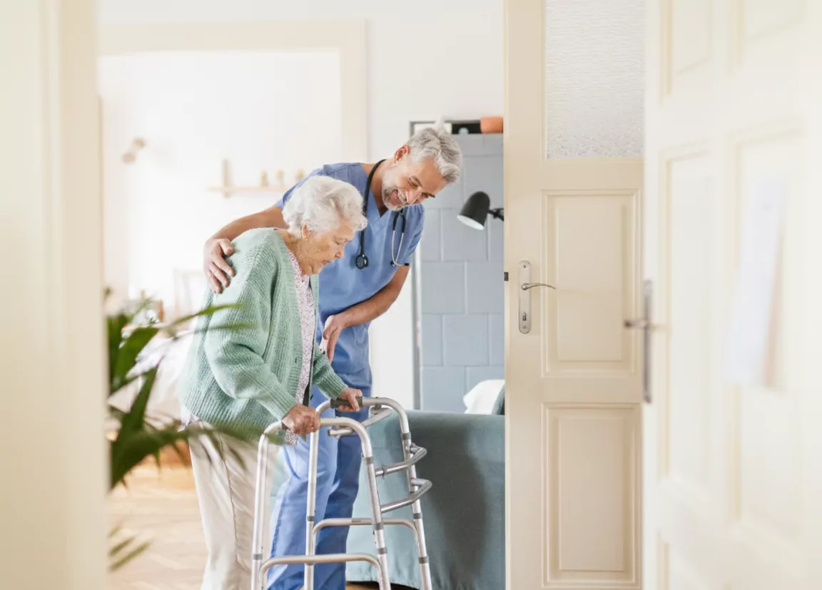 A male carer from Community Care TASMANIA helping an older woman walk with her walking frame